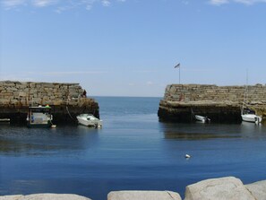 A calm harbor with boats docked at a stone pier, surrounded by calm water and a clear sky.