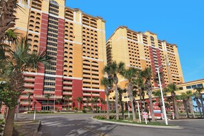 A multi-story hotel with balconies, palm trees, and a clear sky.