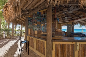 A beachside bar with a wooden exterior, bamboo slats, and a thatched roof.