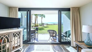Una habitación con televisor, puerta de vidrio que da a un patio con vista al océano y una mesa con sillas.