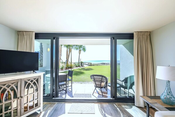 Una habitación con televisor, puerta de vidrio que da a un patio con vista al océano y una mesa con sillas.
