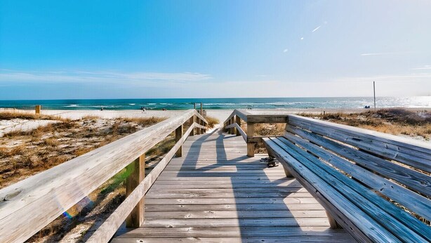 Un paseo marítimo de madera que lleva a una playa, con vista despejada al océano.