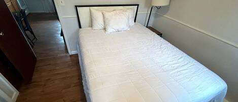 A neatly made bed with a white quilt, a bedside lamp, and a wooden nightstand.