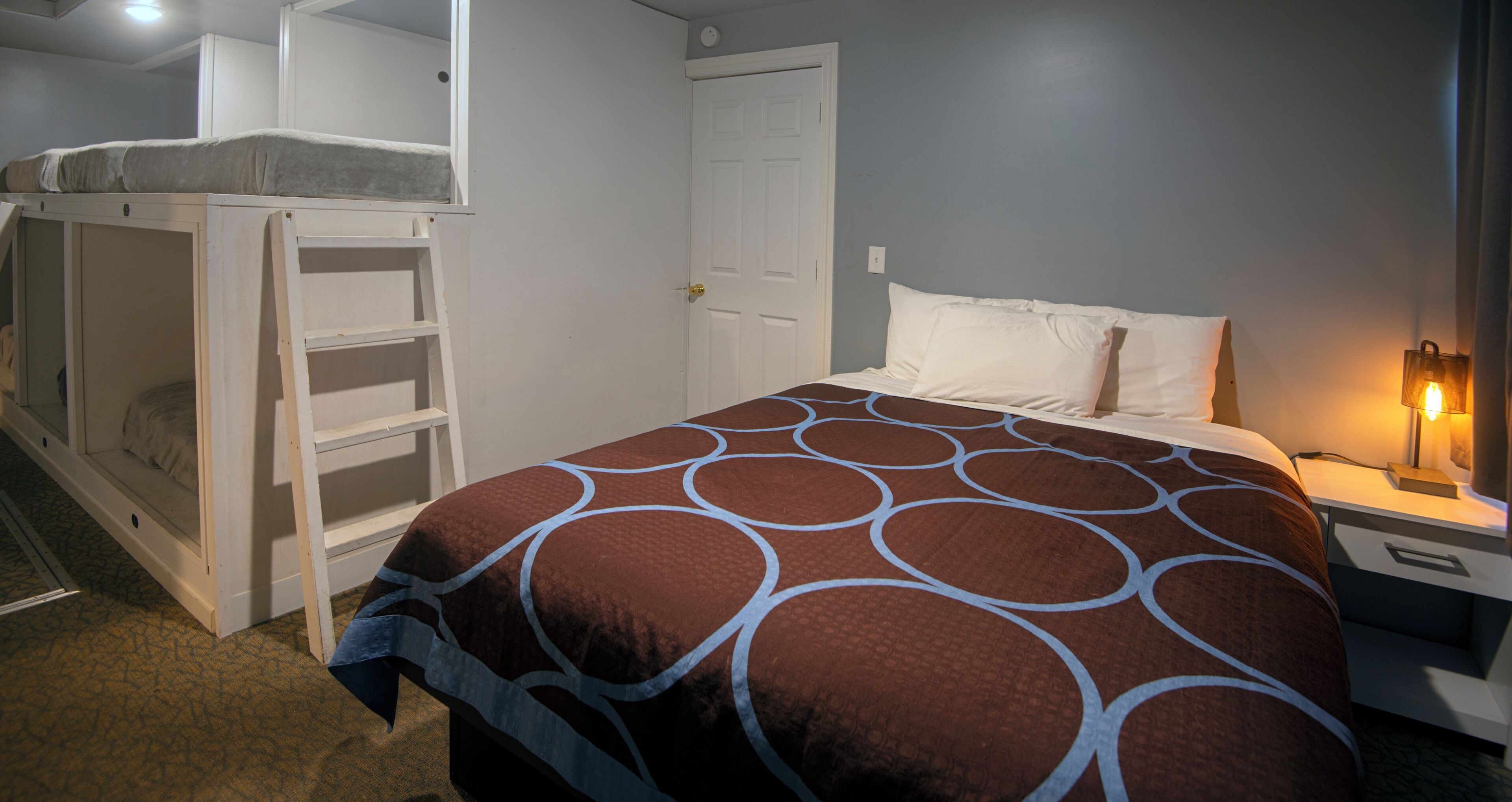 A bedroom with a bunk bed, a single bed, a nightstand, and a lamp.