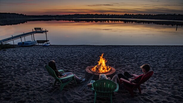 A beach scene with a fire pit and three chairs. - Spirit Lake Resort Motel (Menahga)