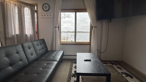 A living room with a sofa, a table, a TV, and a window with a view of a body of water. - Spirit Lake Resort Motel (Menahga)