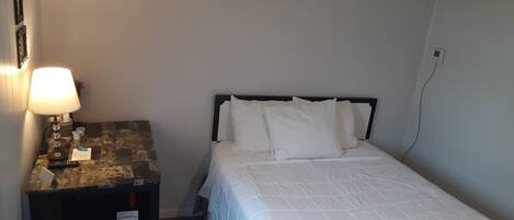 A small, simple room with a bed, a desk, and a chair.