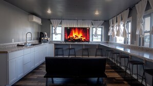 A modern kitchen with a built-in fireplace, white cabinetry, and a bar area with stools. - Spirit Lake Resort Motel (Menahga)