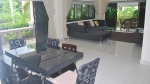 Ein modernes Wohnzimmer mit einem Glastisch, einem schwarzen Sofa und Blick auf üppiges Grün draußen.