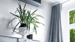 Ein Zimmer mit weißer Wand, einem weißen Schrank, einem Blumentopf, einem grauen Vorhang und einer Klimaanlage.