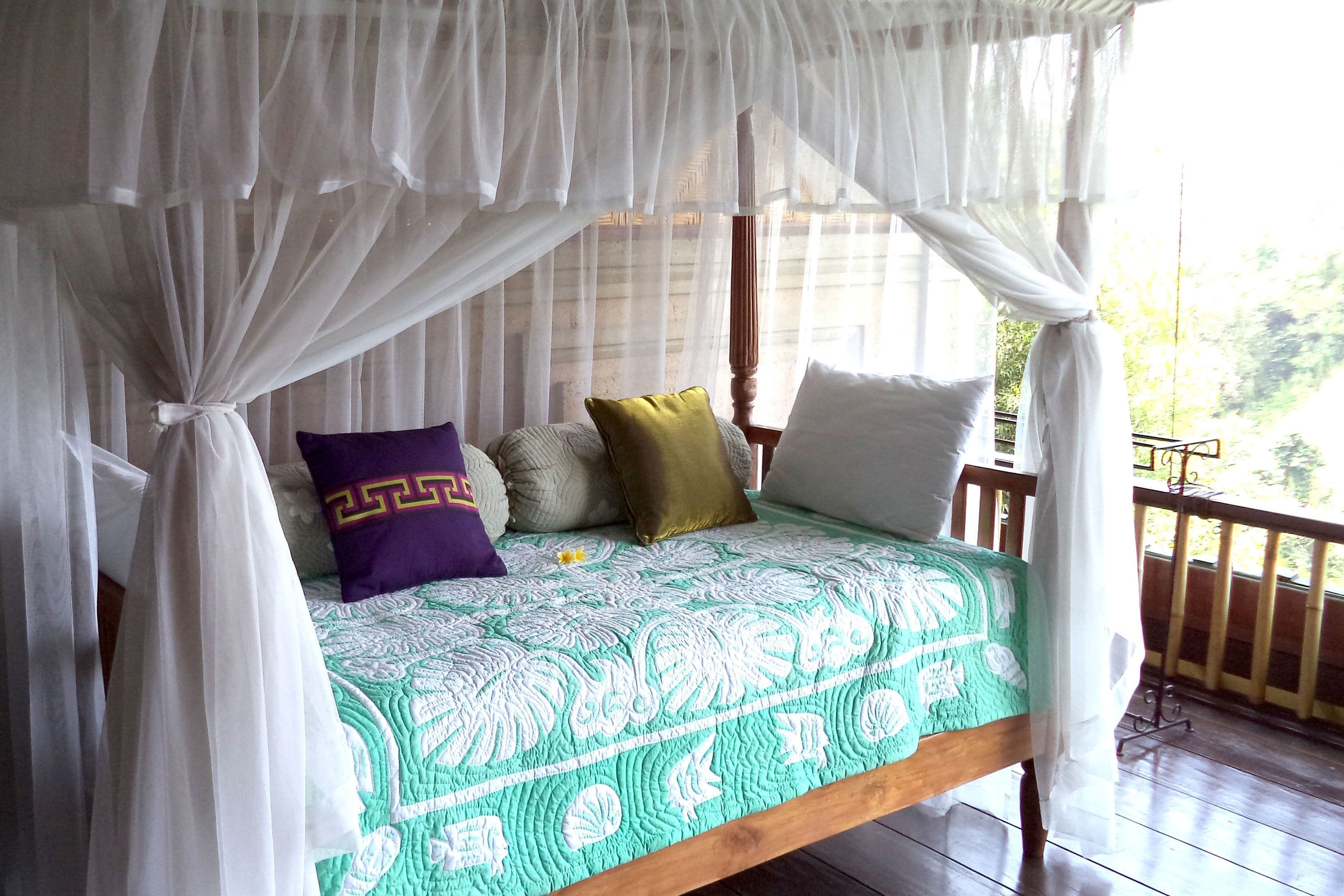 A bed with a canopy, pillows, and a green patterned bedspread.