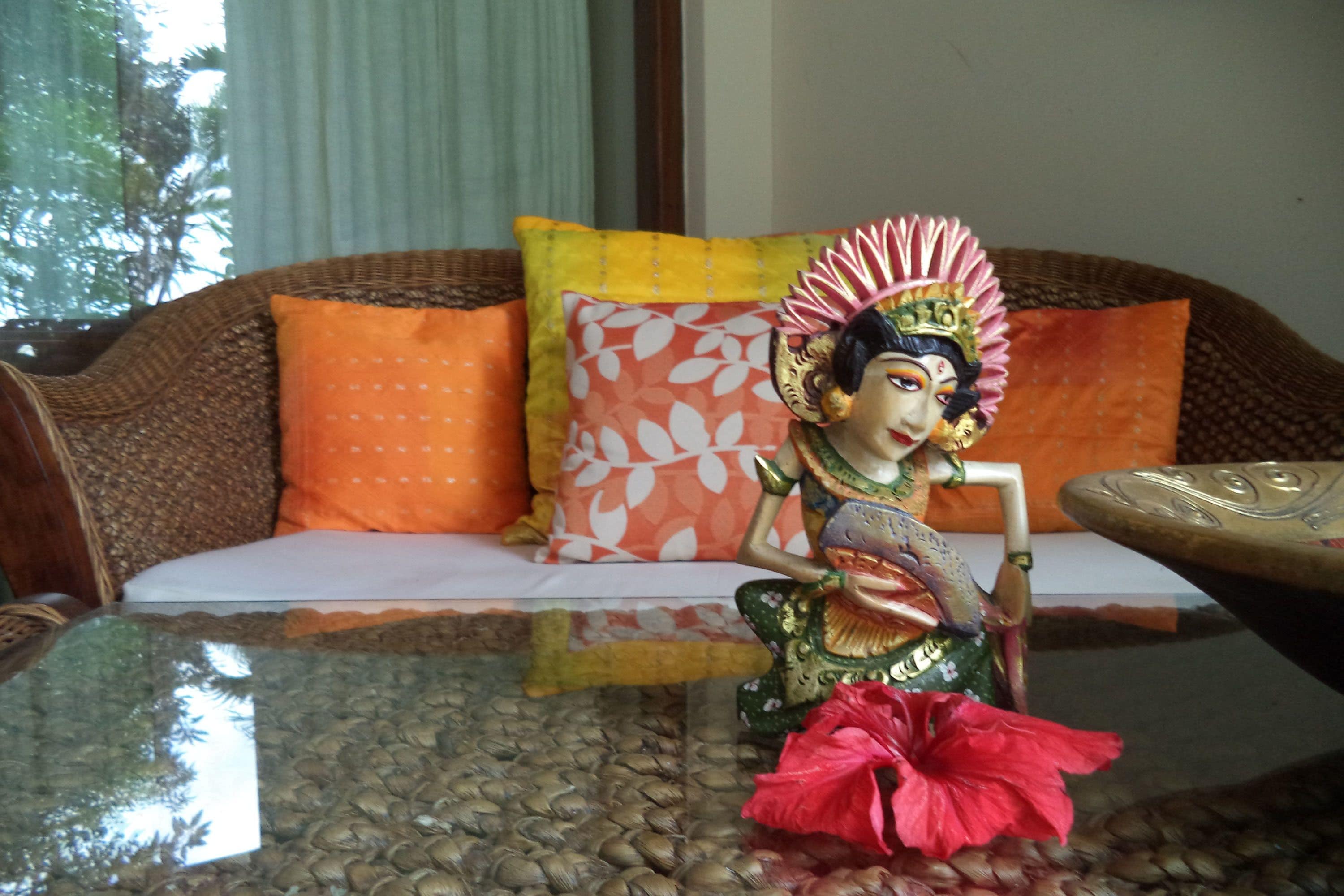 A room with a wicker sofa, a glass coffee table, and a decorative statue.