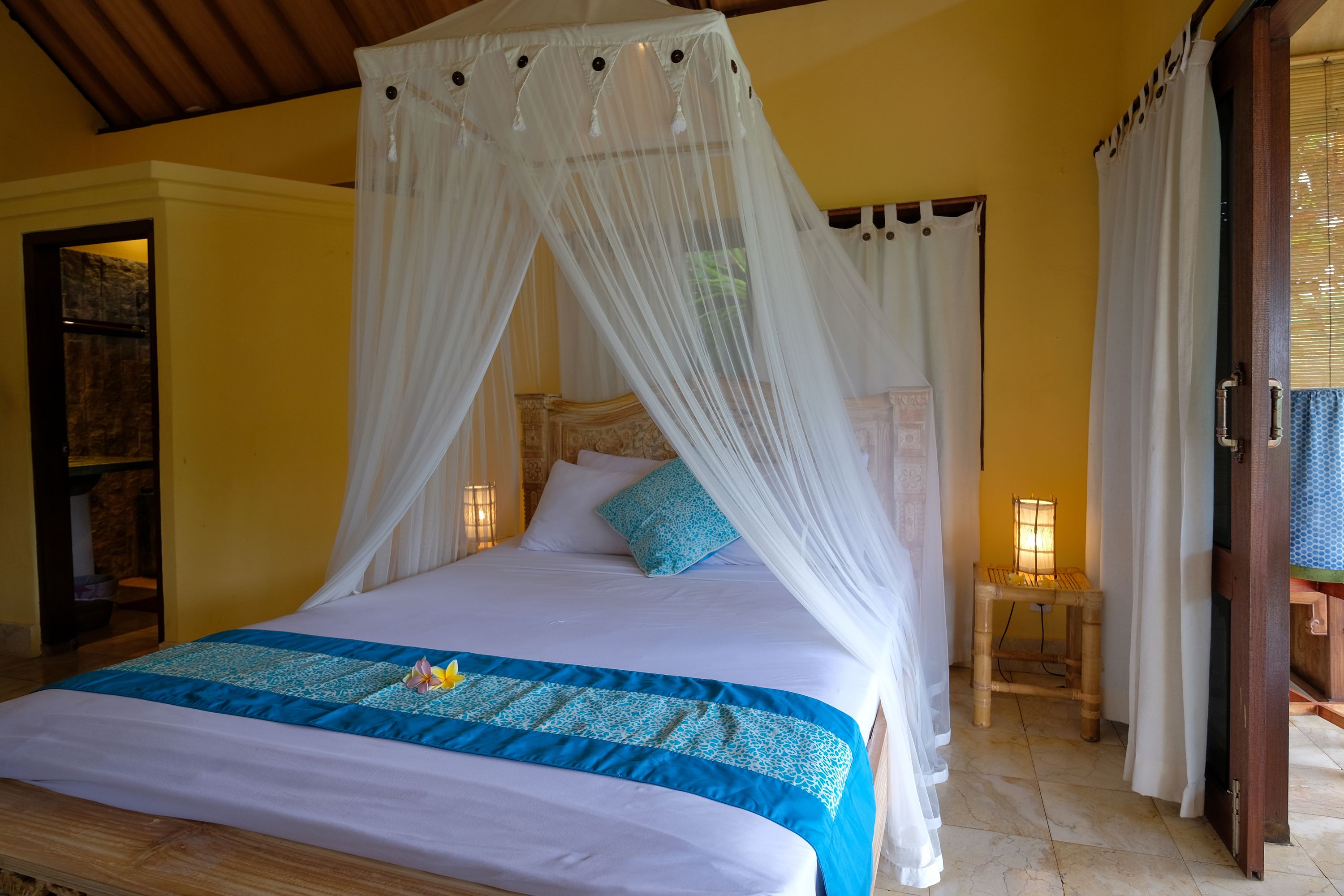 A bed with a canopy, a bedside table with a lamp, and a wooden door.