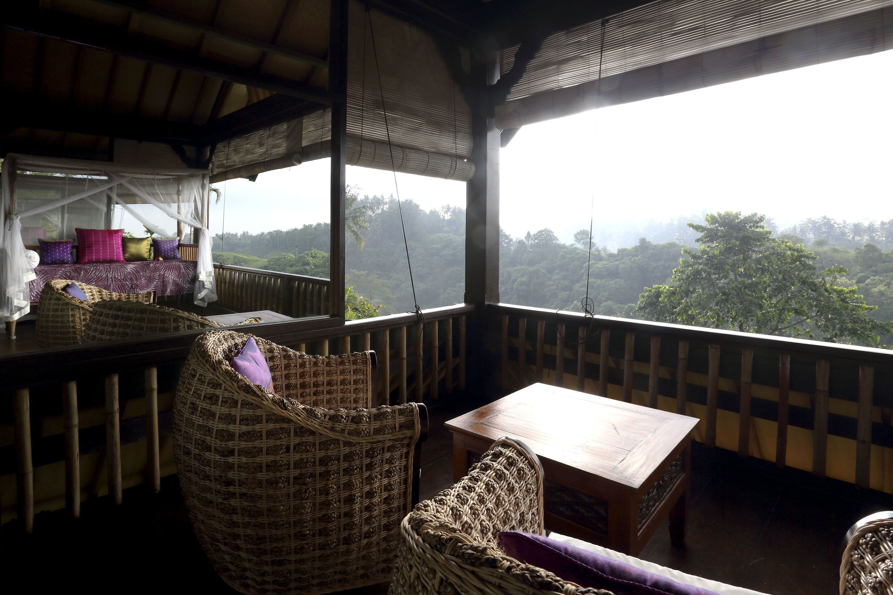 A balcony with wicker furniture, a wooden table, and a view of a forested landscape.