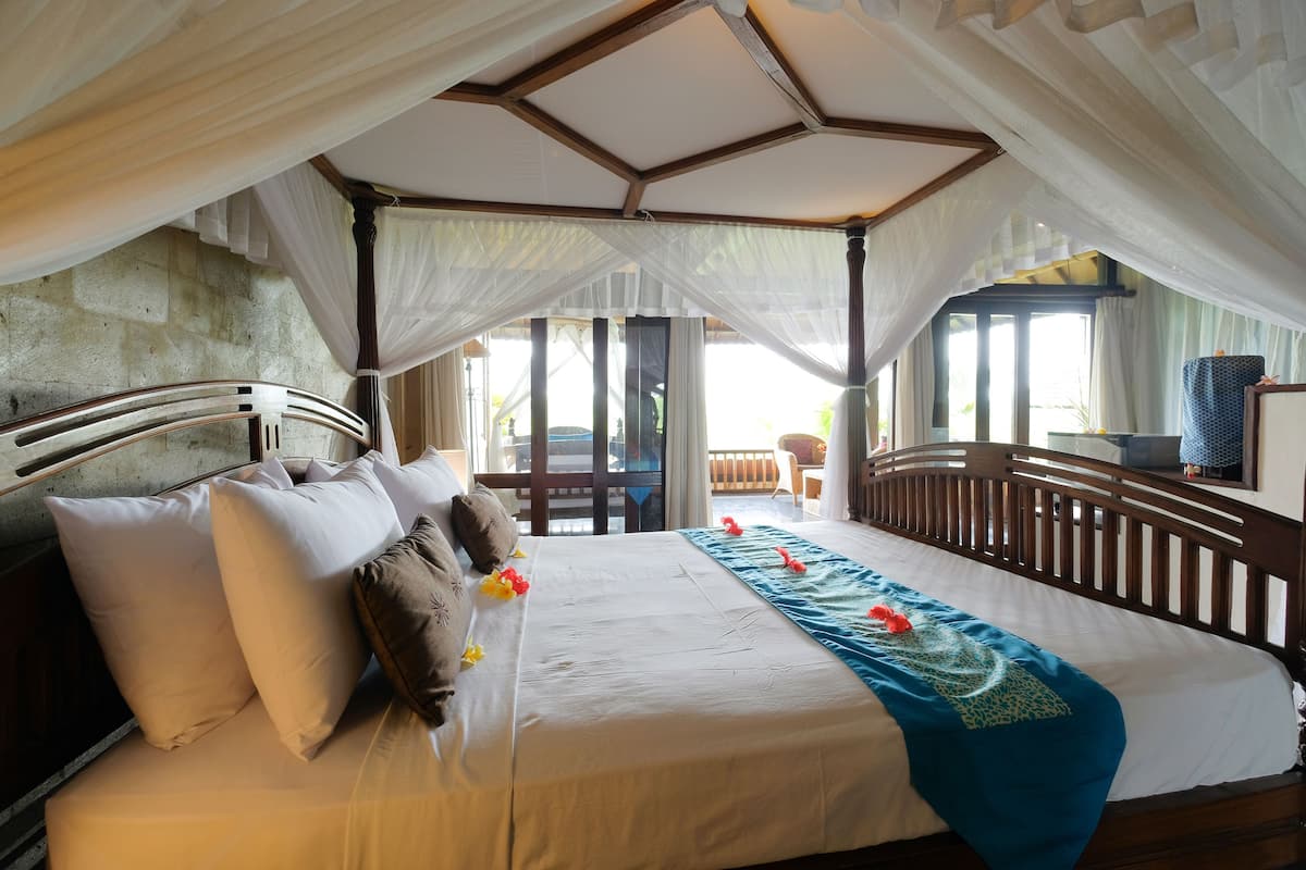 A spacious bedroom with a canopy bed, a balcony view, and a wooden headboard.