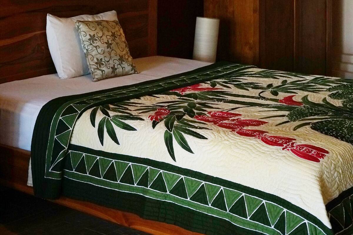 A bed with a canopy, a wooden headboard, and a green and white quilt.