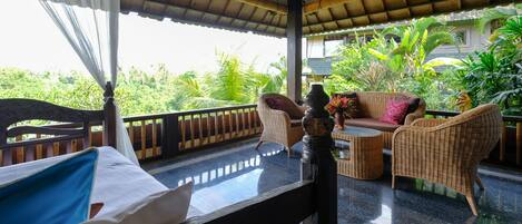 A room with a bed, wicker furniture, and a view of lush greenery.