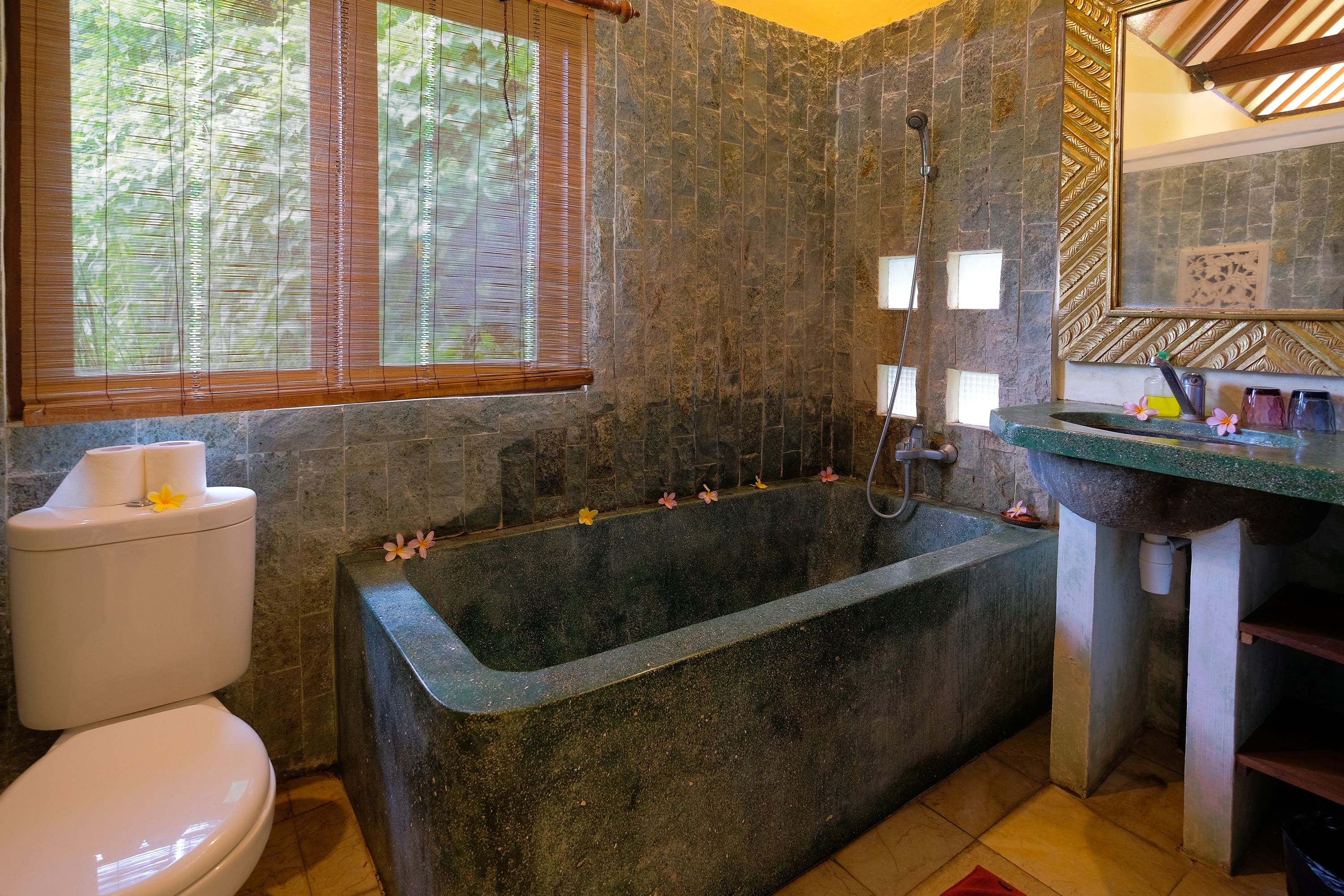 Une salle de bain avec un mur en pierre, une baignoire, des toilettes et un lavabo.
