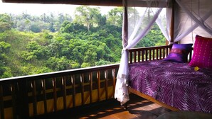 A room with a bed, a view of a forest, and a balcony with a wooden railing. - Sunrise Villa Ubud (Ubud)