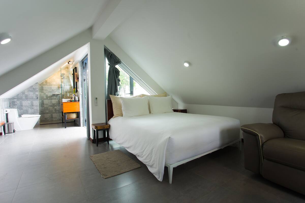 A bedroom with a large bed, a sofa, and a bathroom visible through an open door.