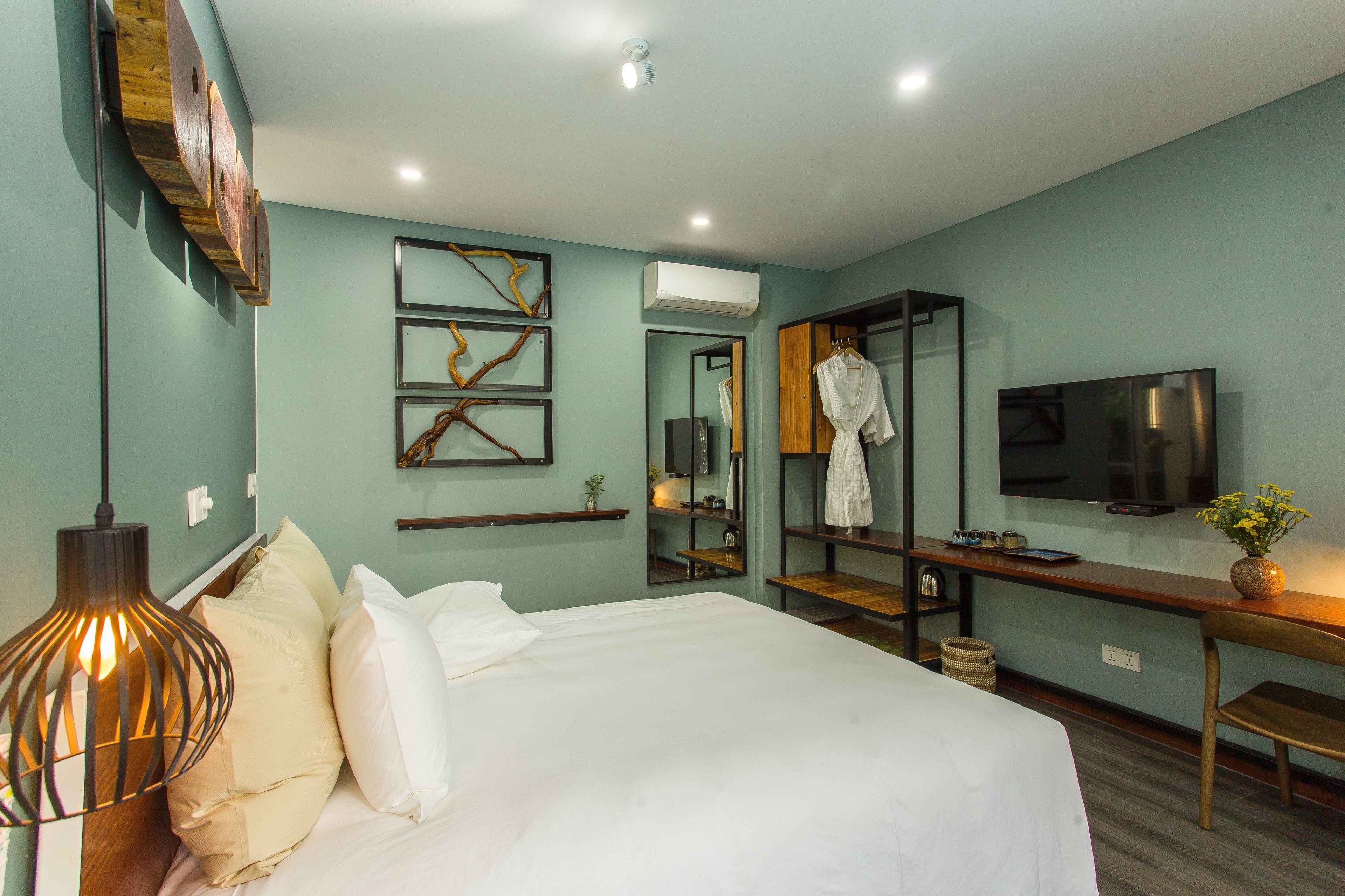 A modern hotel room with a large bed, a desk with a flat-screen TV, a mirror, and artwork on the walls.