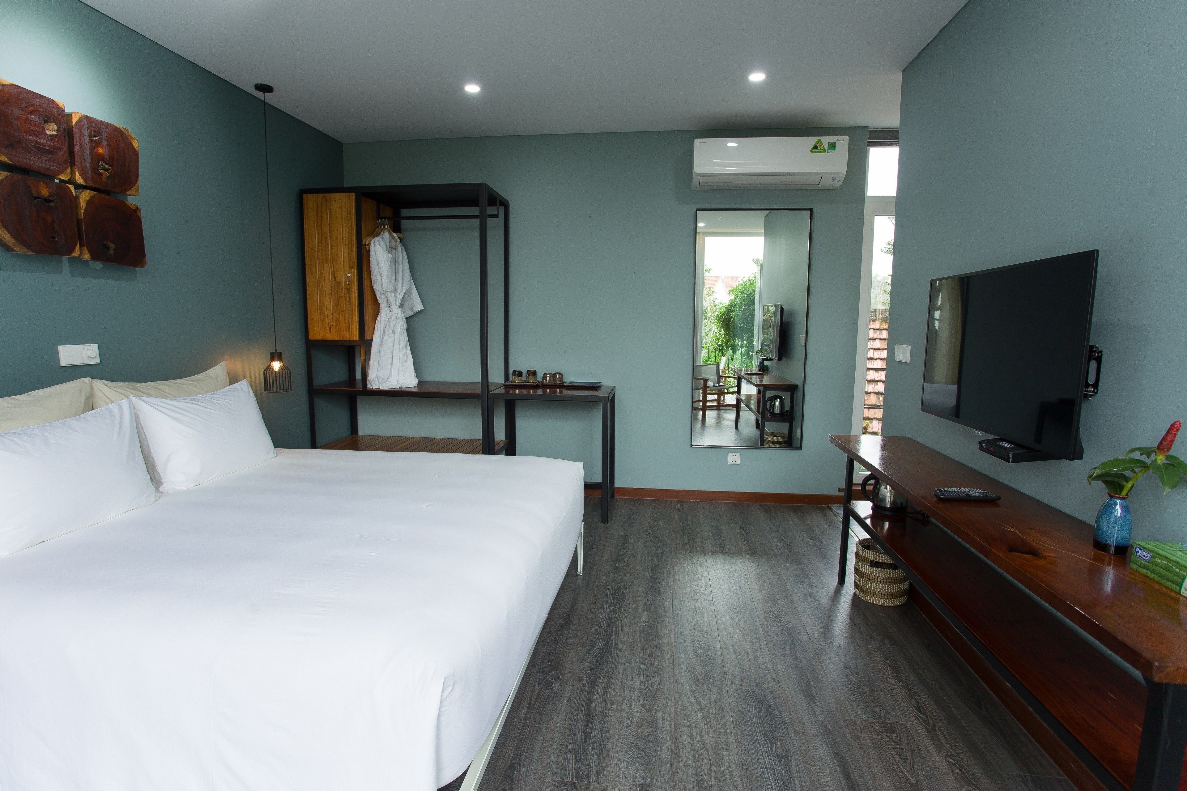 A hotel room with a bed, a wooden bench, a TV, and a mirror.