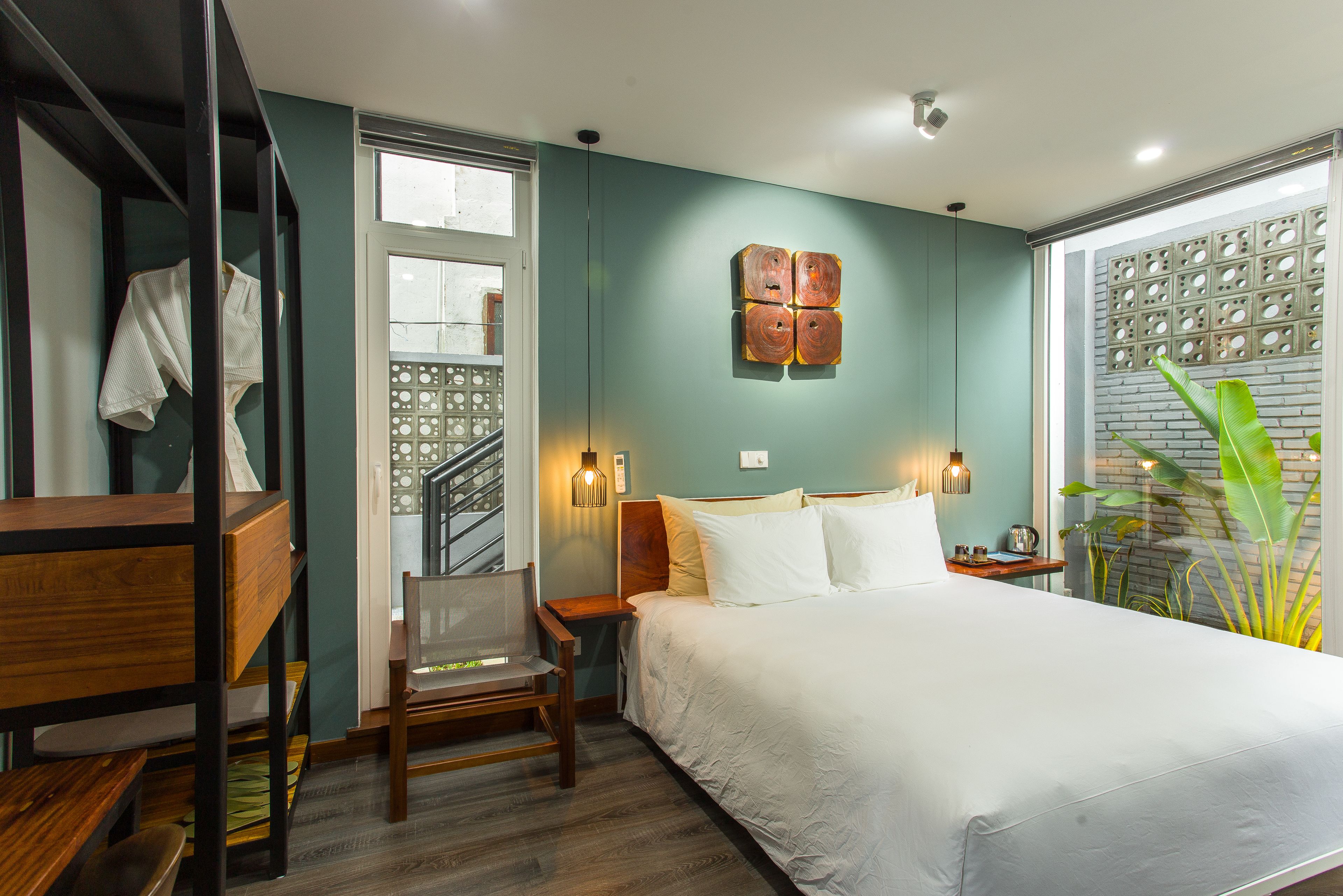 A bedroom with a bed, a desk, a chair, a nightstand, and a wall-mounted light fixture.