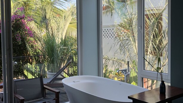 A modern bathroom with a freestanding bathtub, large windows, and a view of a tropical garden. - Chay Villas An Bang (Da Nang)
