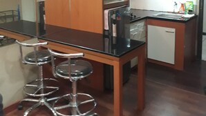 Een compacte keuken met een zwart aanrecht, roestvrijstalen apparatuur en een kleine koelkast. Er staan twee barkrukken bij het aanrecht.