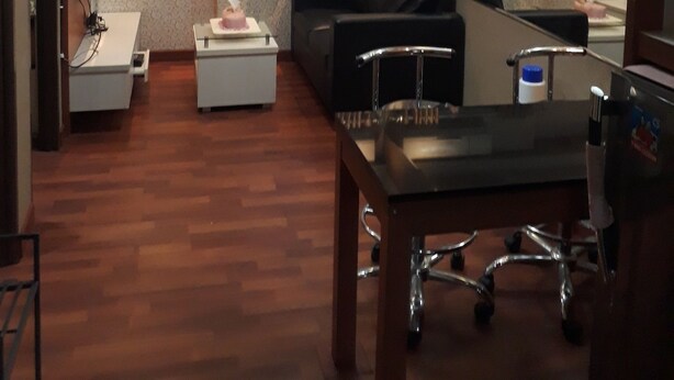 Een hotelkamer met een houten vloer, een zwarte leren bank, een klein wit tafeltje, een glazen salontafel, een bureau met een computer, en een televisie aan de rechter muur.