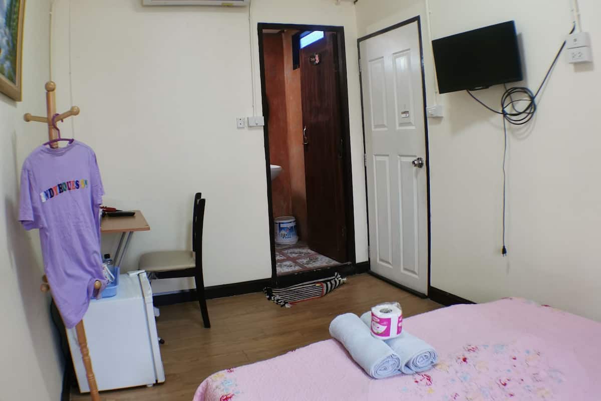 A bedroom with a bed, a desk, a chair, a TV, and an air conditioner.