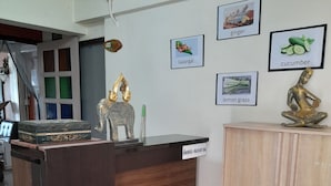 A reception desk with a wooden finish and an orange circle sticker. There are framed pictures on the wall depicting ginger, cucumber, galangal, and lemon grass. - 59 Indy House  (Bangkok)