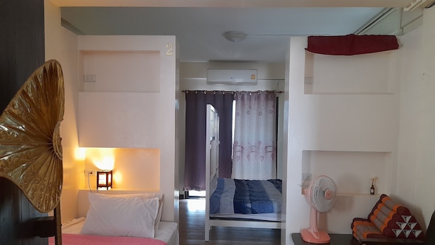 A room with a bed, a desk, a chair, a fan, and a window with curtains. - 59 Indy House  (Bangkok)