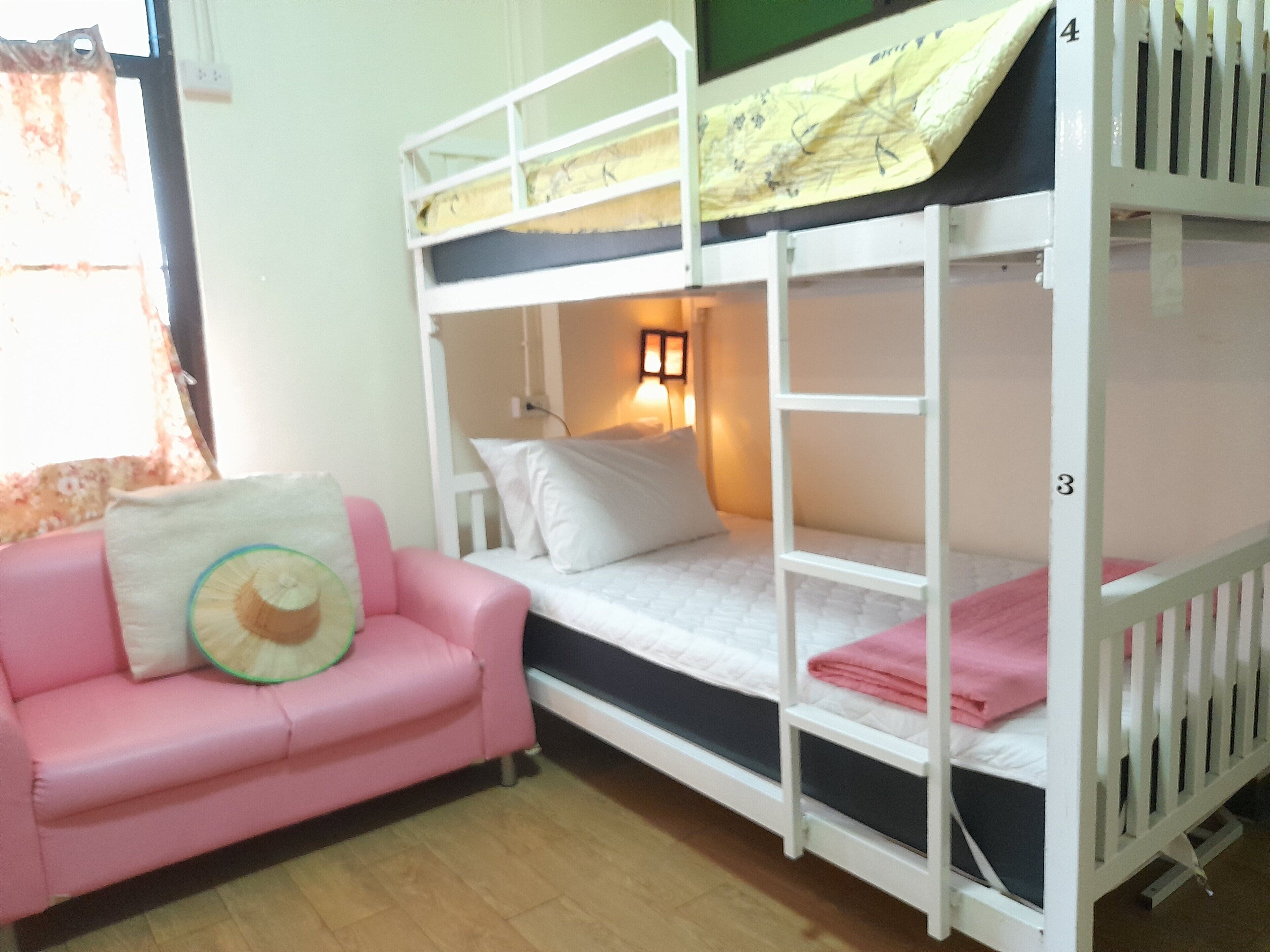 A bunk bed with a desk and chair, a pink sofa, and a lamp.
