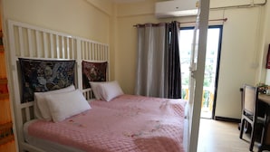 A bedroom with a bed, a white headboard, a window with curtains, and a view of the outside. - 59 Indy House  (Bangkok)