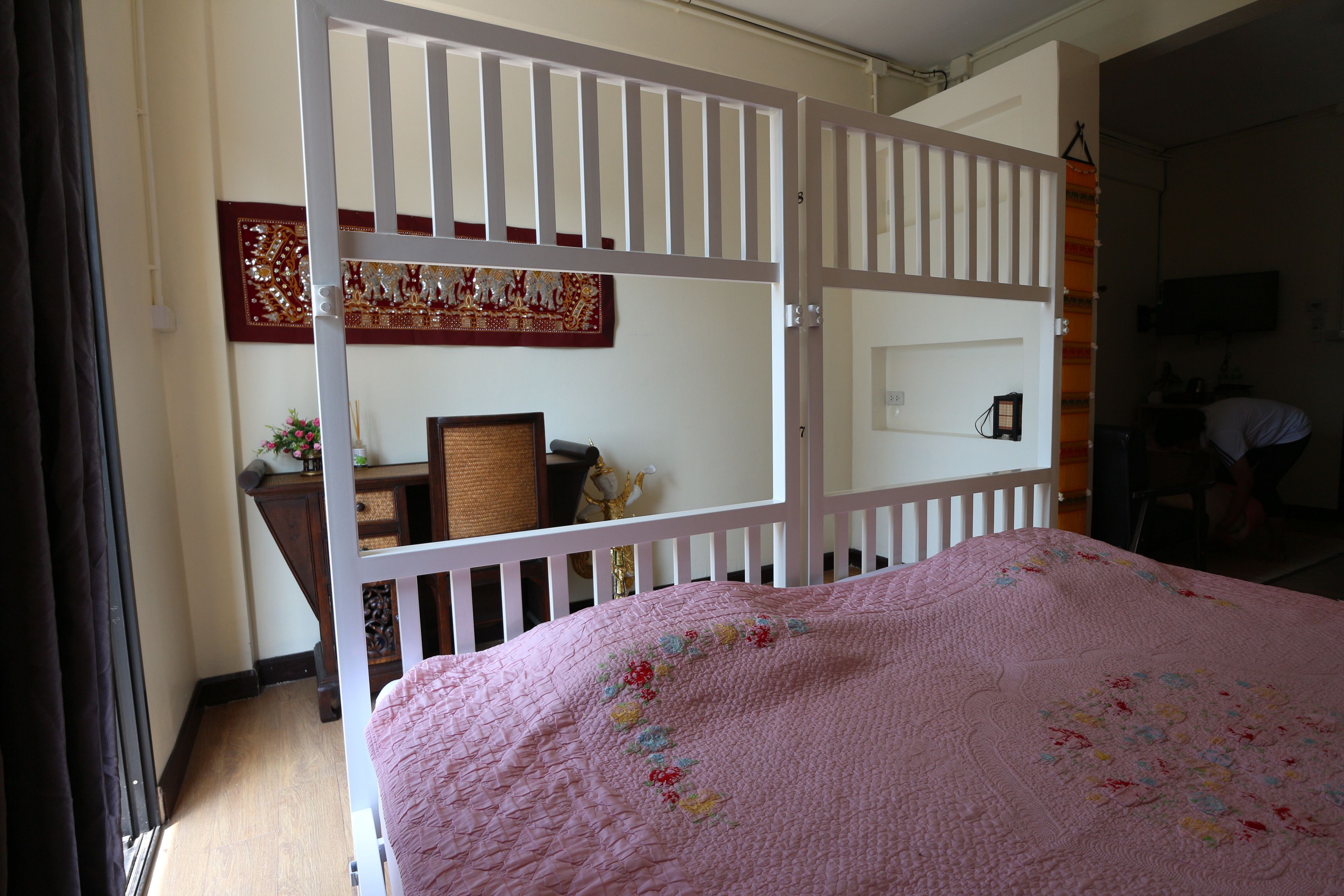 Une chambre à coucher avec une couverture de lit rose matelassée, un berceau blanc et un bureau en bois avec une chaise.