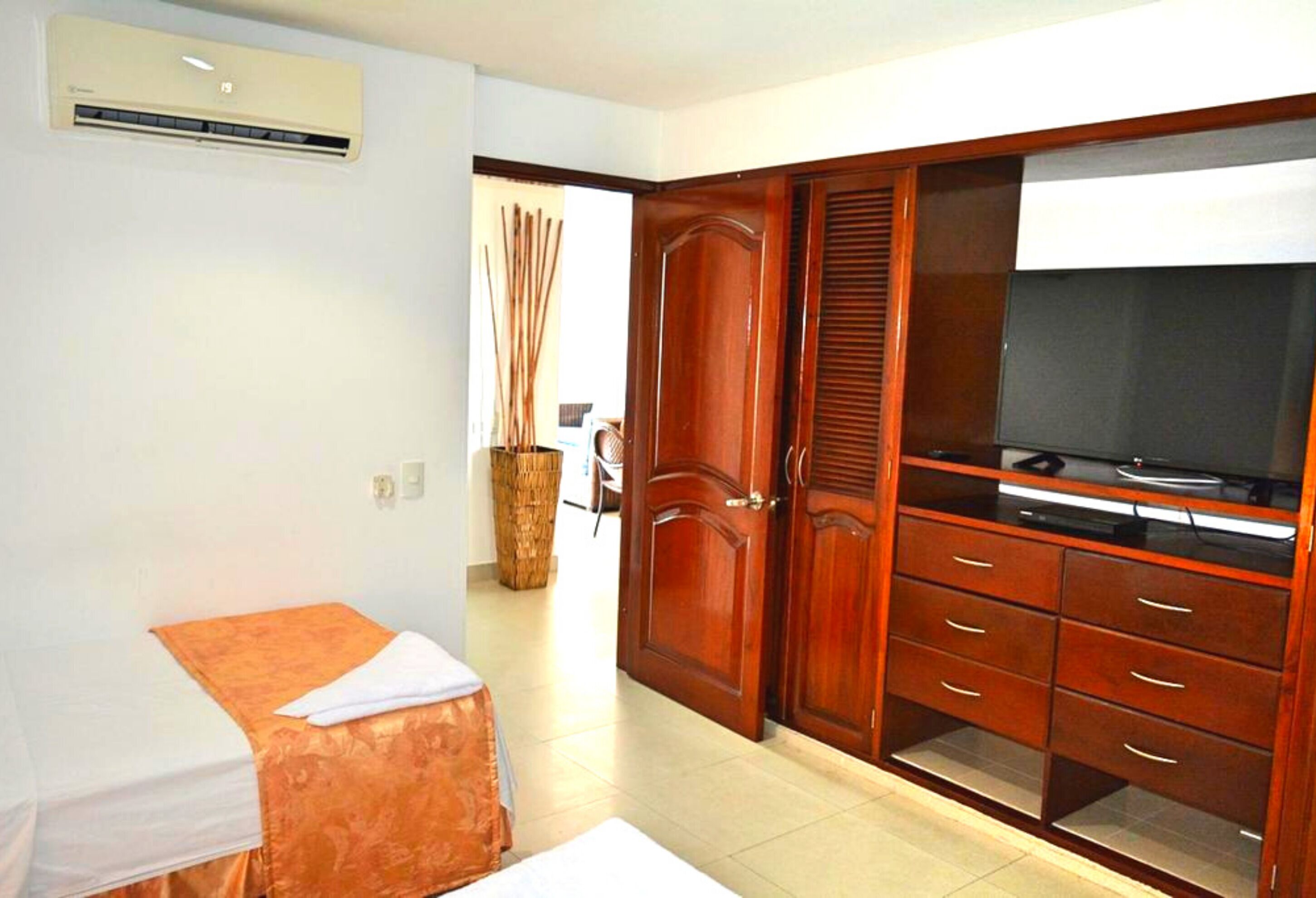 A hotel room with a bed, wardrobe, television, and an air conditioning unit.
