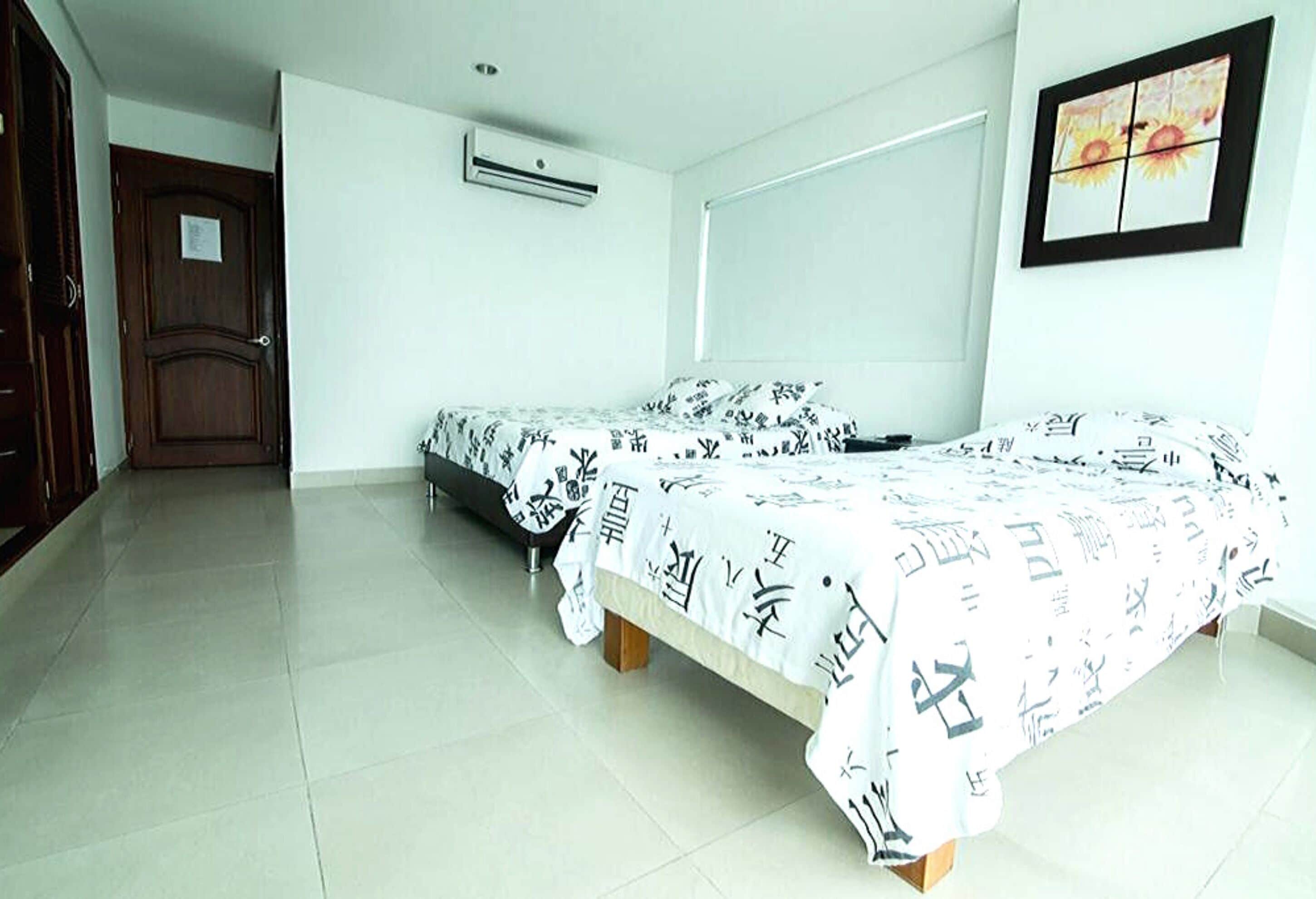 A bedroom with two beds, a door, an air conditioning unit, and a framed picture on the wall.