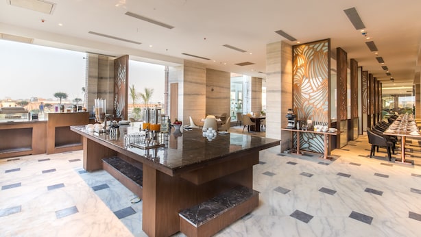 Un hall d’hôtel moderne doté d’un grand comptoir de réception en marbre, d’un espace salon et de panneaux décoratifs.