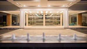 L’entrée d’un hôtel moderne, agrémentée d’un élément décoratif aquatique à l’avant, de portes en verre et d’un intérieur bien éclairé.