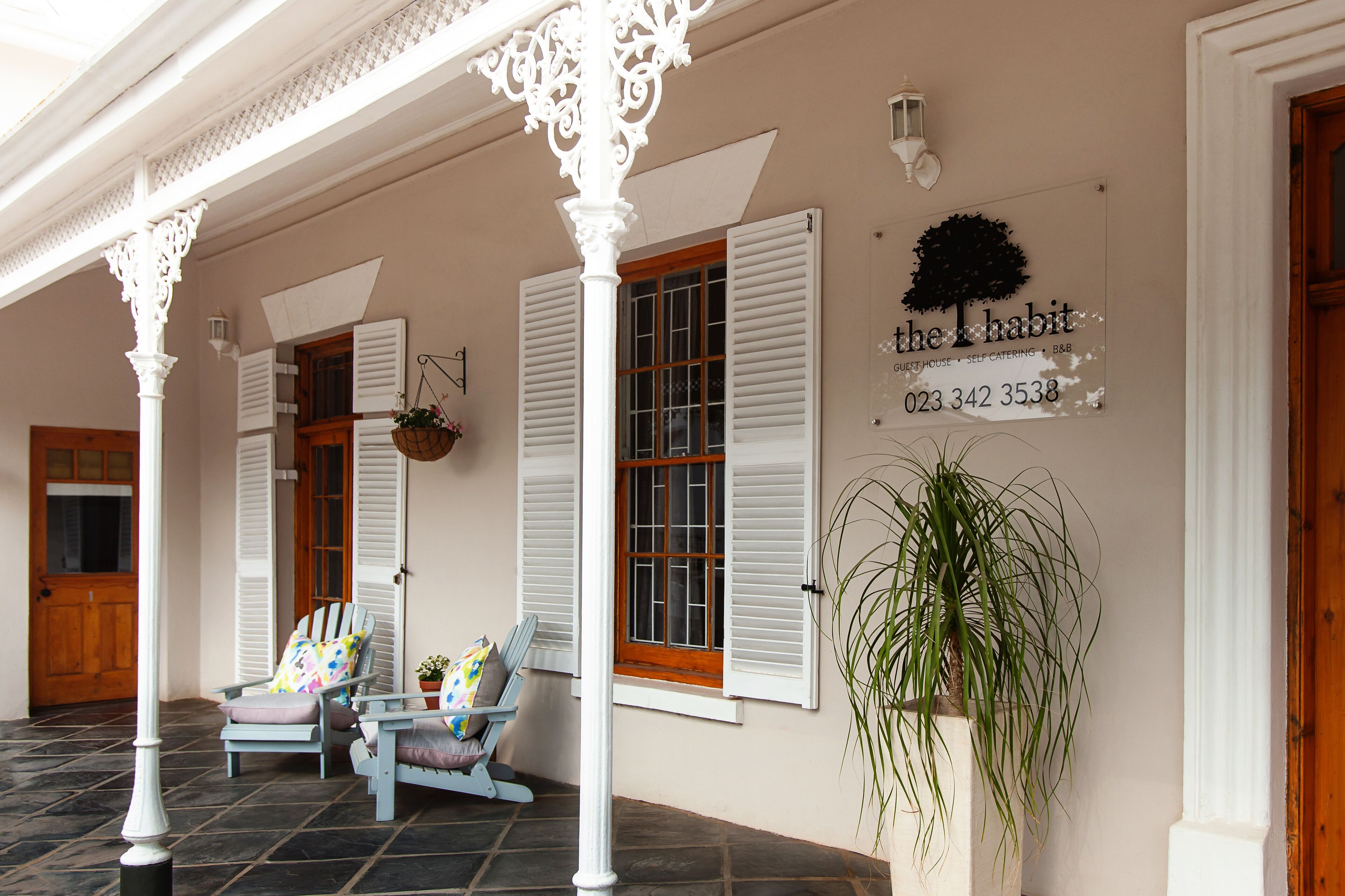 A covered porch with white columns, two rocking chairs, and a sign reading "the habit" with a phone number.