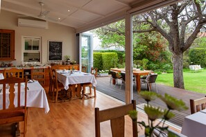 A restaurant with wooden furniture, a chalkboard with 'Enjoy your breakfast' message, and a view of a tree and garden through large glass doors. - The Habit Guest House (Worcester)
