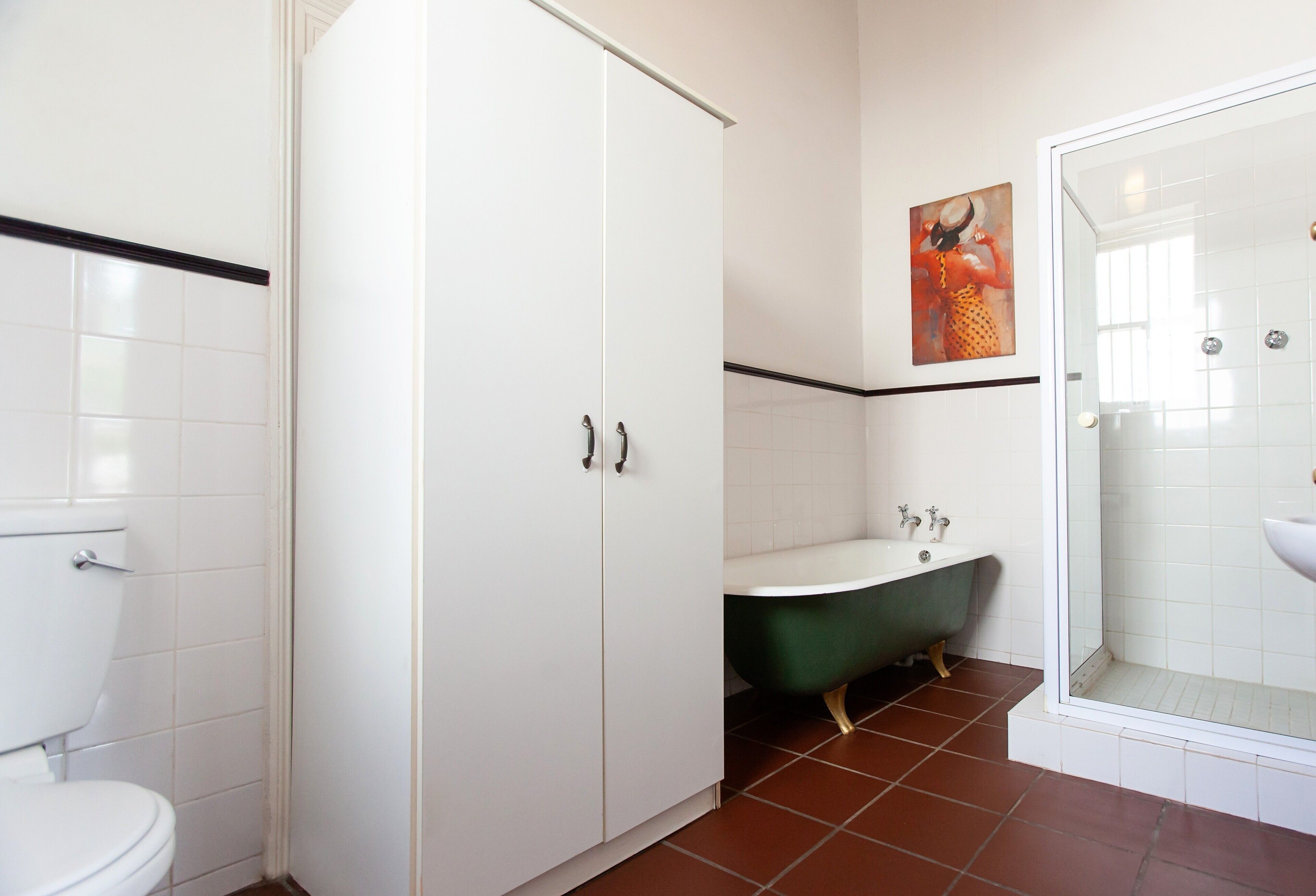 Un bagno con il water, una vasca da bagno verde con piedi a zampa di leone, una doccia e un armadietto bianco.