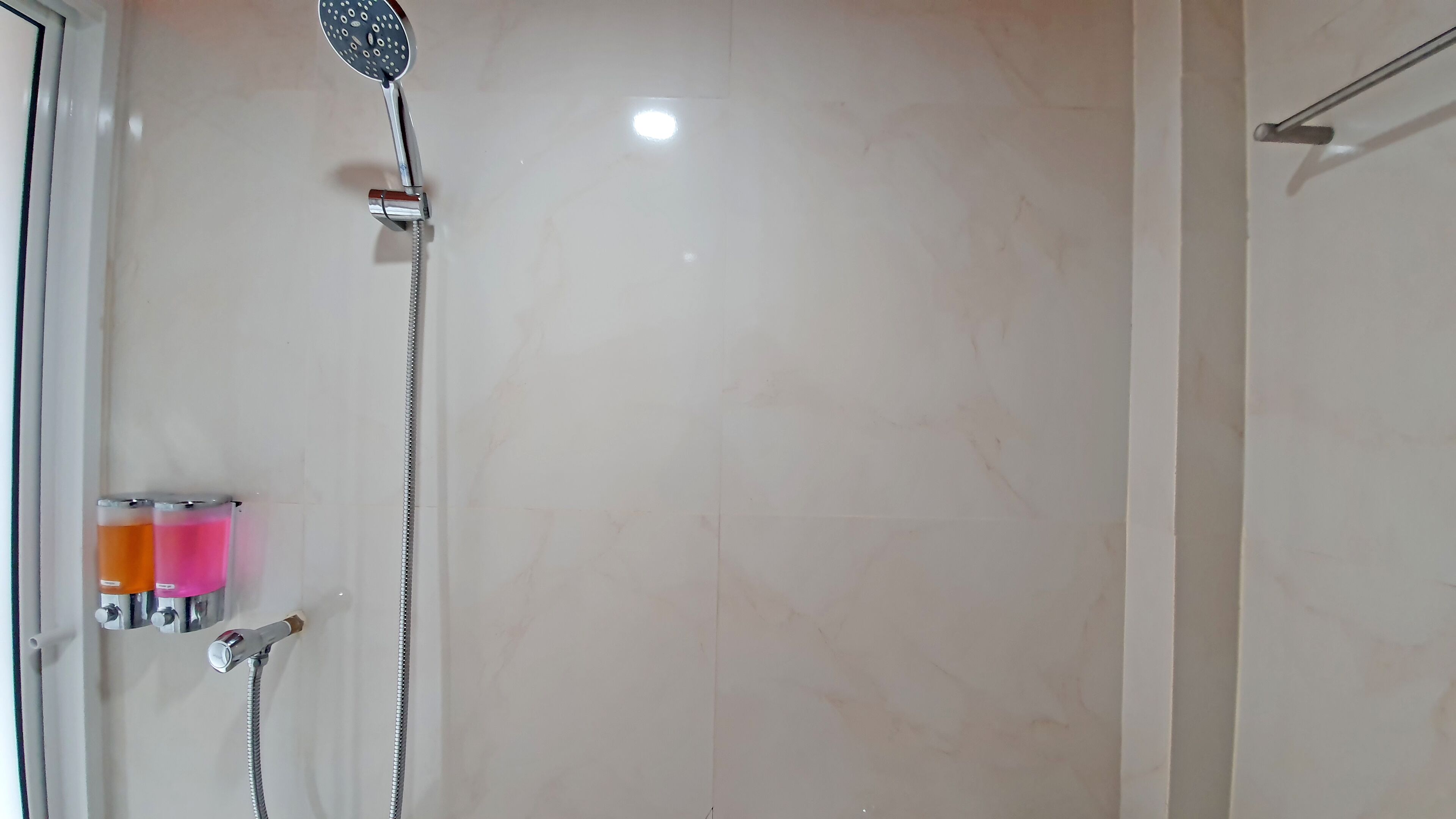 A bathroom with a shower, a mirror, and two bottles of shampoo.