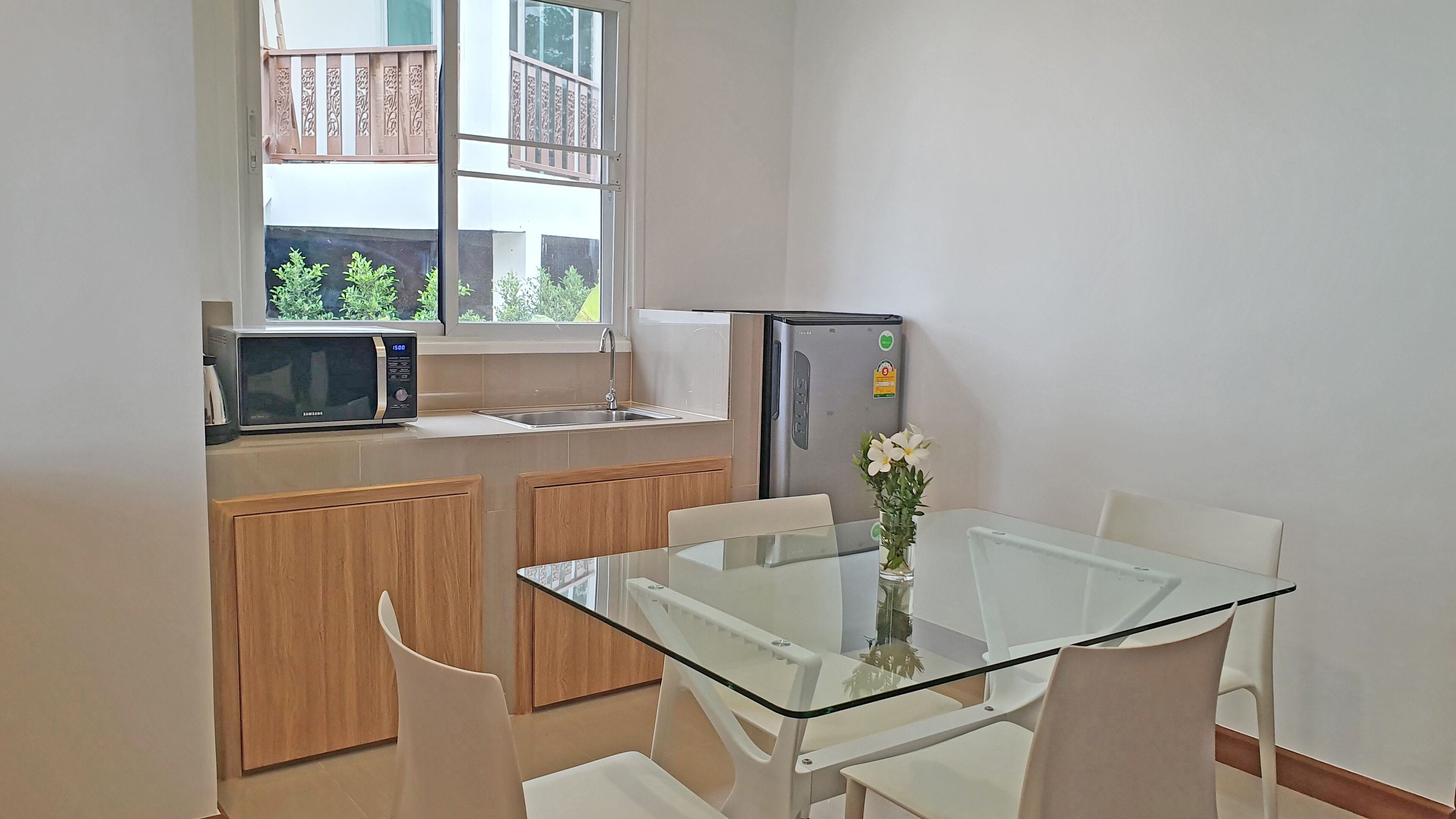 A compact kitchen with a microwave, refrigerator, and a small dining area with a glass table and chairs.