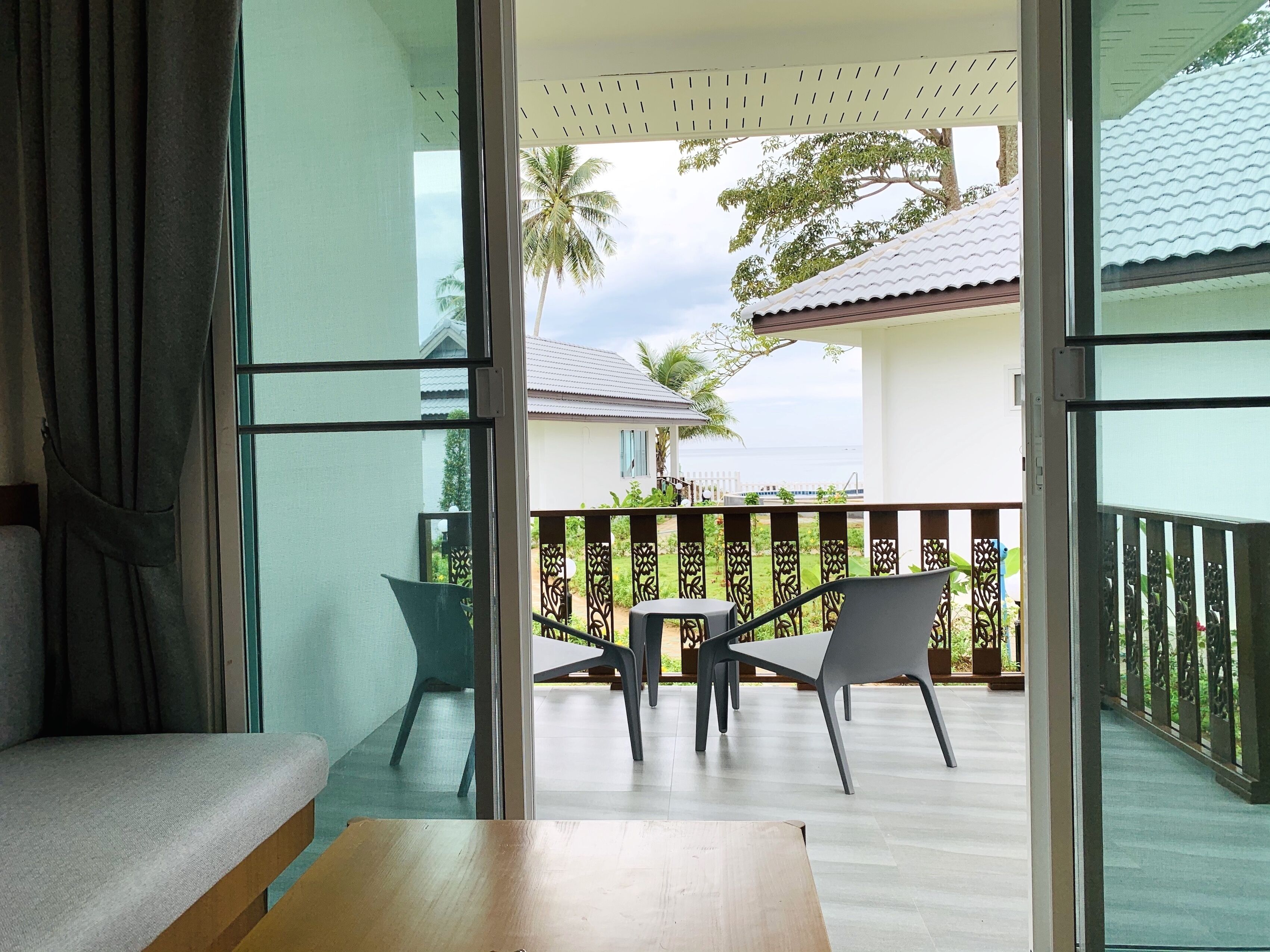 A balcony with a wooden table and two chairs, a sofa, and a view of a white building and palm trees.