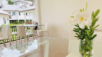 A modern room with a glass table, white chairs, a vase with white flowers, and a view of a white building with a tiled roof.