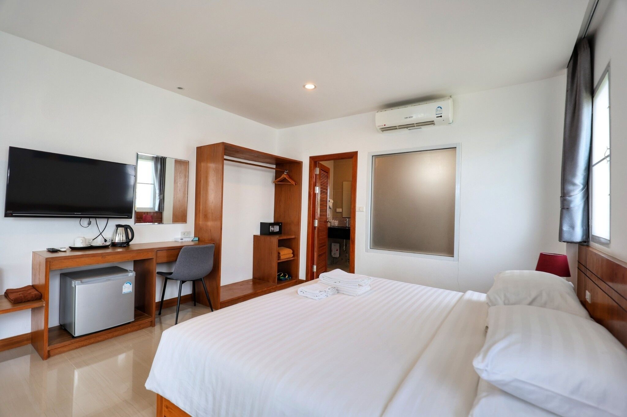 Ein Hotelzimmer mit Bett, Schreibtisch mit Computer, Fernseher, Minikühlschrank, Kleiderschrank und Klimaanlage.