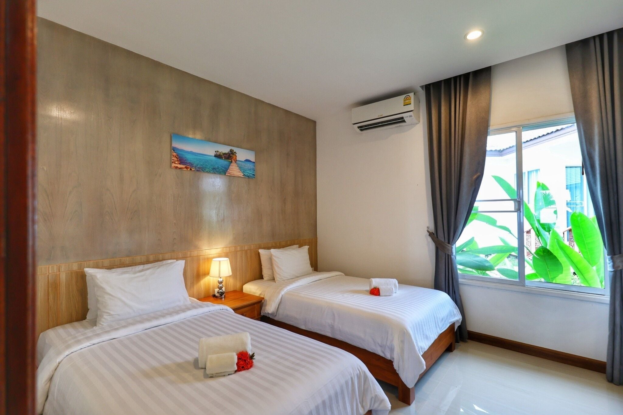A hotel room with two beds, a painting on the wall, an air conditioning unit, and a window with curtains.