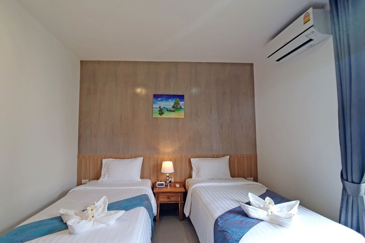 Een hotelkamer met twee bedden, een nachtkastje met een lamp, een schilderij aan de muur en een airconditioning.
